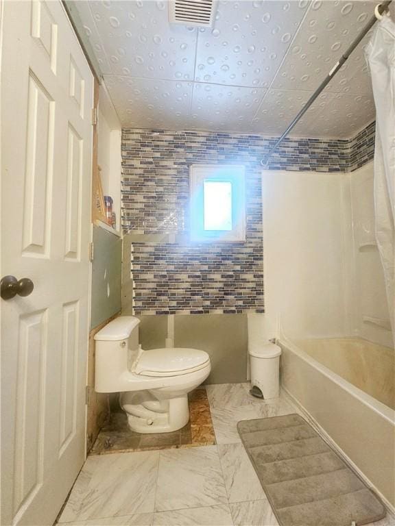 bathroom with toilet, tile walls, and shower / bath combo with shower curtain