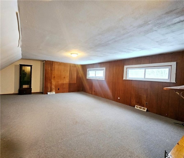 bonus room featuring carpet floors, a textured ceiling, wooden walls, and vaulted ceiling