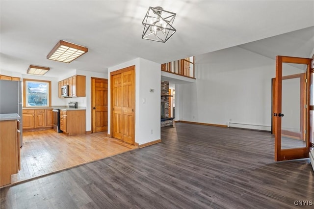 kitchen featuring hanging light fixtures, a brick fireplace, baseboard heating, wood-type flooring, and stainless steel appliances