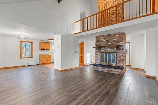 unfurnished living room featuring a brick fireplace, hardwood / wood-style floors, a high ceiling, and a baseboard heating unit