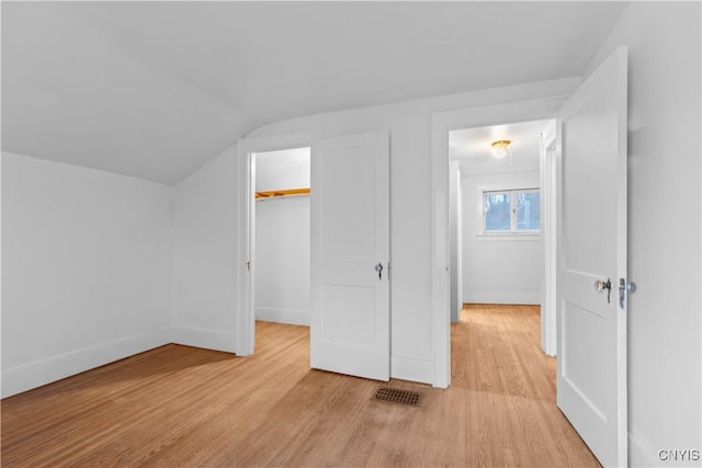 unfurnished bedroom featuring a spacious closet, vaulted ceiling, light wood-type flooring, and a closet