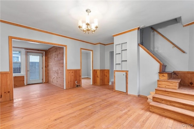 unfurnished living room featuring a chandelier, wood walls, ornamental molding, and light hardwood / wood-style flooring