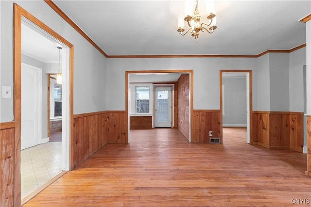 empty room featuring wooden walls, ornamental molding, light hardwood / wood-style floors, and a notable chandelier