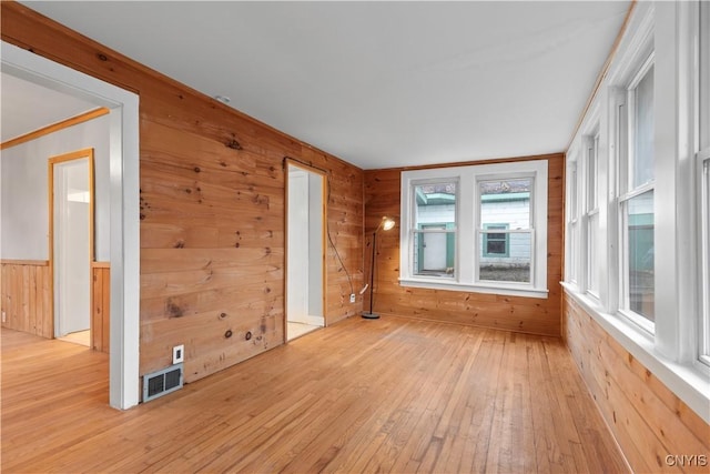 empty room with wood walls, crown molding, and light wood-type flooring