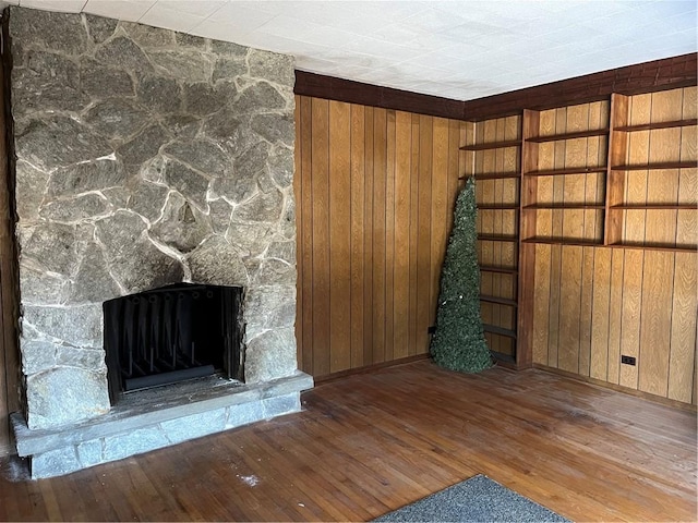 unfurnished living room featuring a stone fireplace, wooden walls, and hardwood / wood-style floors