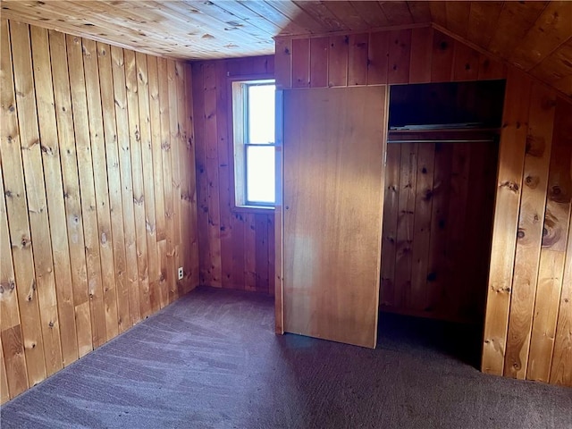 interior space featuring dark colored carpet, lofted ceiling, wooden walls, a closet, and wood ceiling