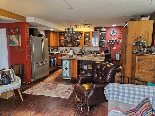 kitchen with dark hardwood / wood-style floors, decorative backsplash, light stone countertops, a kitchen island, and stainless steel refrigerator