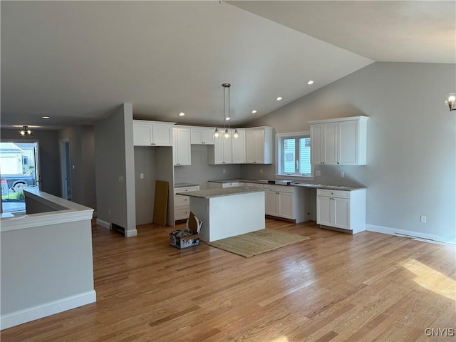 kitchen featuring lofted ceiling, light wood-type flooring, decorative light fixtures, a kitchen island, and white cabinetry