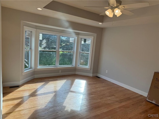 empty room with a tray ceiling, ceiling fan, and light wood-type flooring