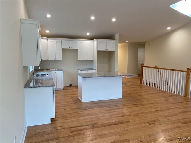 kitchen with sink, dark stone countertops, a center island, light hardwood / wood-style floors, and white cabinetry