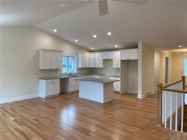 kitchen featuring white cabinets, light hardwood / wood-style flooring, a kitchen island, and lofted ceiling