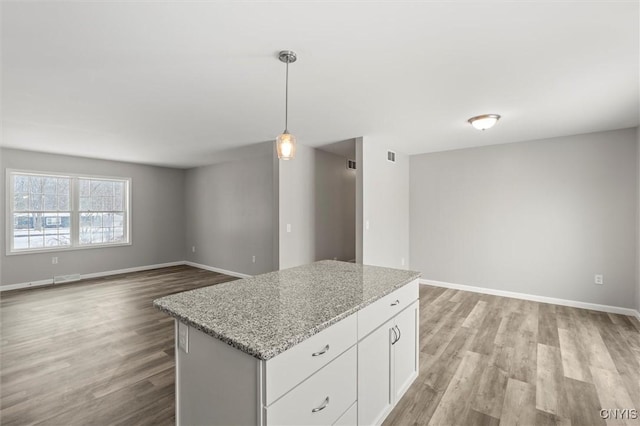 kitchen with hanging light fixtures, white cabinets, light stone counters, a kitchen island, and light wood-type flooring