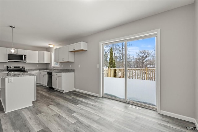 kitchen with white cabinetry, light stone counters, light hardwood / wood-style floors, pendant lighting, and appliances with stainless steel finishes