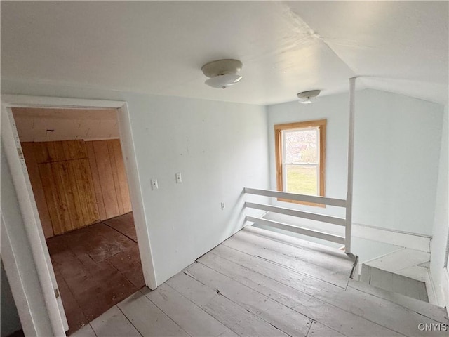 corridor featuring light hardwood / wood-style flooring, vaulted ceiling, and wood walls