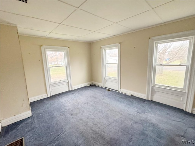 empty room featuring dark colored carpet, a drop ceiling, and a wealth of natural light