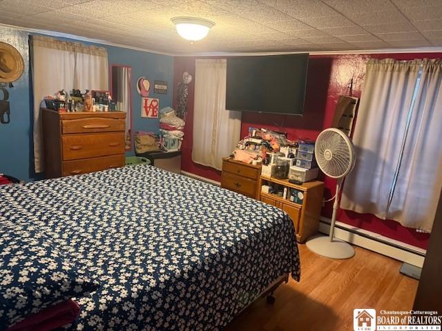 bedroom featuring hardwood / wood-style floors, a baseboard heating unit, and ornamental molding