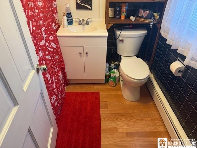 bathroom featuring vanity, toilet, tile walls, a baseboard radiator, and wood-type flooring