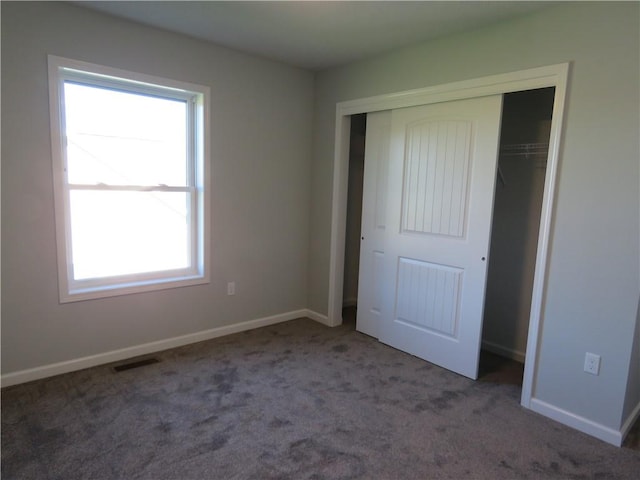 unfurnished bedroom featuring multiple windows, a closet, and dark colored carpet