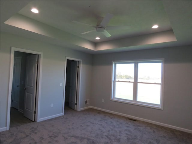 unfurnished bedroom featuring ceiling fan, a raised ceiling, and light carpet