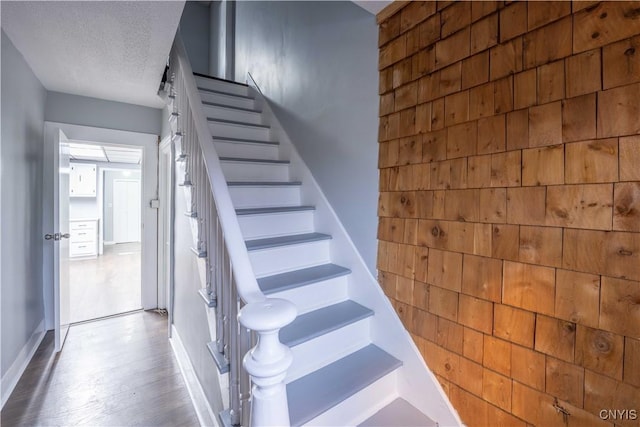 stairway with wood-type flooring, a textured ceiling, and wooden walls