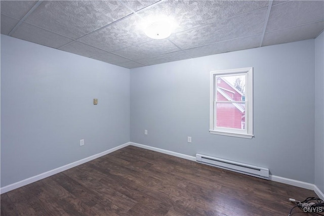 empty room with a drop ceiling, dark hardwood / wood-style floors, and a baseboard heating unit