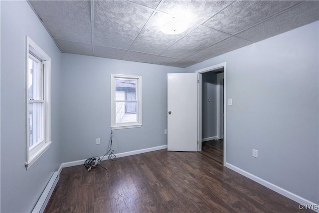 spare room featuring a drop ceiling, baseboard heating, and dark wood-type flooring