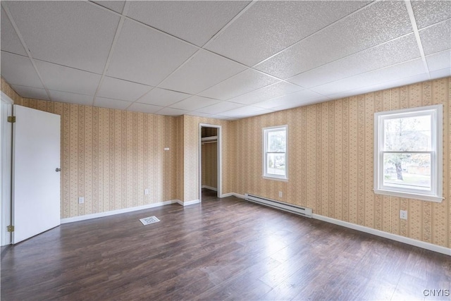 empty room with a paneled ceiling, dark hardwood / wood-style floors, a healthy amount of sunlight, and baseboard heating