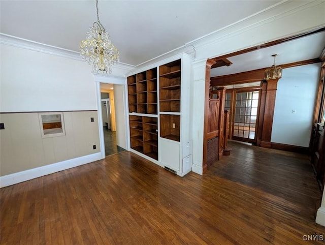 empty room with built in features, ornamental molding, dark wood-type flooring, and an inviting chandelier