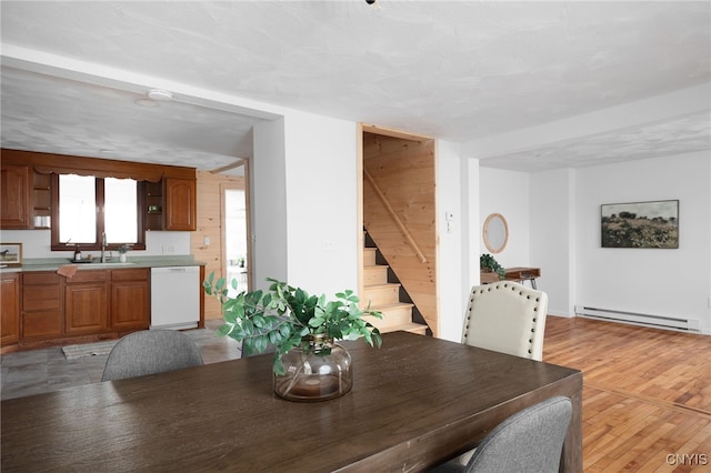 dining area with wood walls, sink, light wood-type flooring, a textured ceiling, and a baseboard radiator