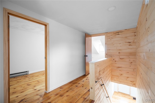 hall featuring wood walls, light hardwood / wood-style floors, and a baseboard heating unit