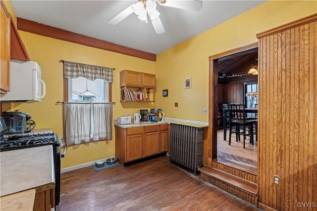 kitchen featuring radiator, ceiling fan, dark wood-type flooring, gas range oven, and wooden walls