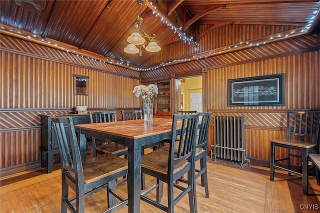 dining room with wood walls, lofted ceiling, radiator, an inviting chandelier, and wood ceiling