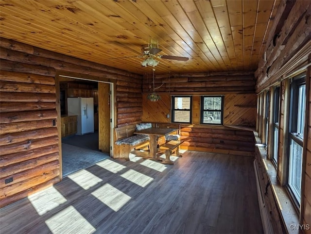 interior space featuring ceiling fan, rustic walls, wooden ceiling, and dark wood-type flooring