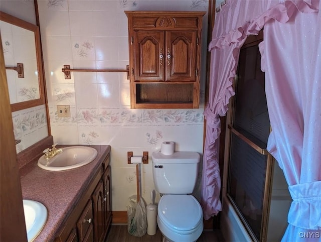 full bathroom with combined bath / shower with glass door, vanity, toilet, and tile walls