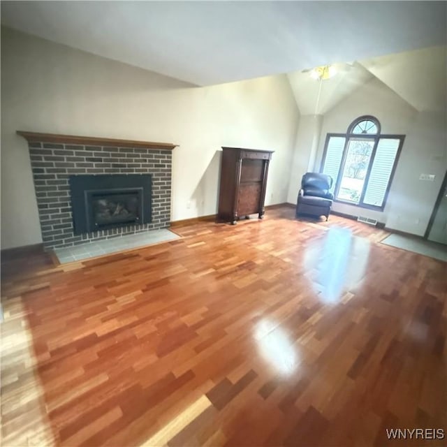 unfurnished living room with a tile fireplace, wood-type flooring, and lofted ceiling