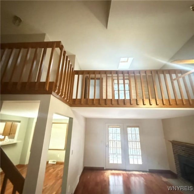 unfurnished living room featuring a skylight, hardwood / wood-style floors, a high ceiling, and a brick fireplace