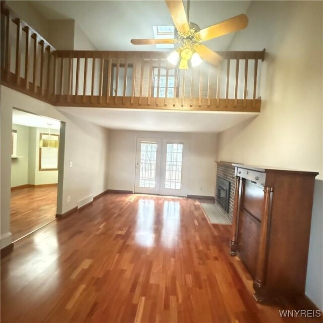 unfurnished living room featuring ceiling fan, wood-type flooring, a towering ceiling, and a brick fireplace