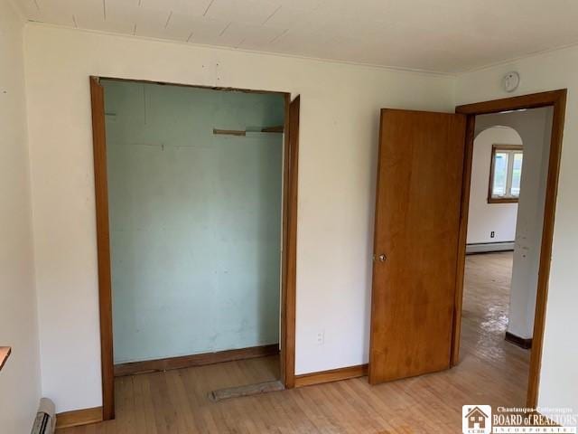 unfurnished bedroom with light hardwood / wood-style flooring, a closet, and a baseboard heating unit