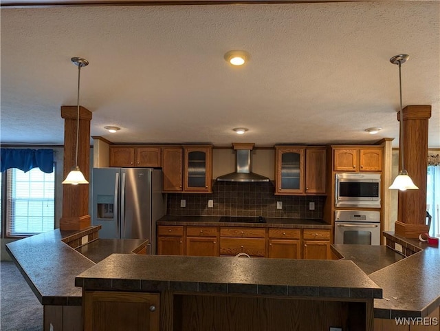 kitchen with backsplash, stainless steel appliances, hanging light fixtures, and wall chimney range hood