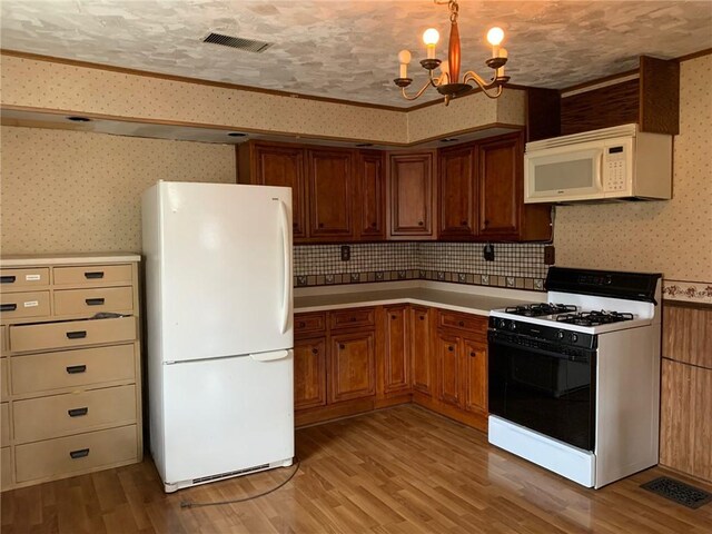 kitchen featuring light wood-type flooring, ornamental molding, a textured ceiling, white appliances, and a notable chandelier