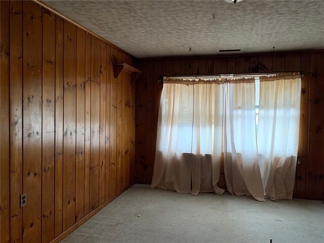 carpeted empty room with a textured ceiling and wooden walls