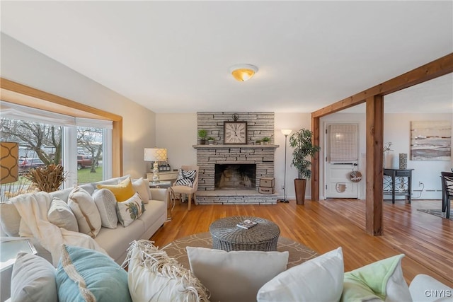 living room with a stone fireplace, a baseboard heating unit, and light wood-type flooring