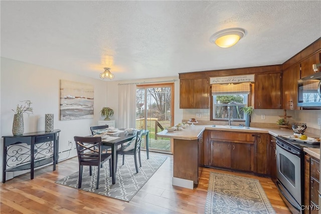 kitchen featuring sink, backsplash, light hardwood / wood-style floors, a textured ceiling, and appliances with stainless steel finishes