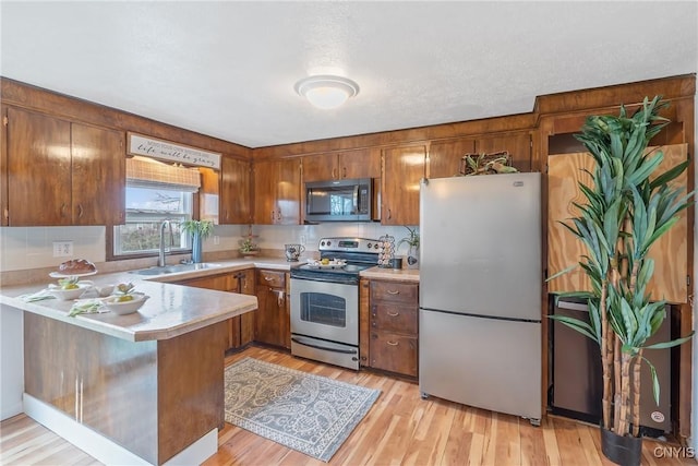 kitchen with kitchen peninsula, a textured ceiling, stainless steel appliances, sink, and light hardwood / wood-style floors