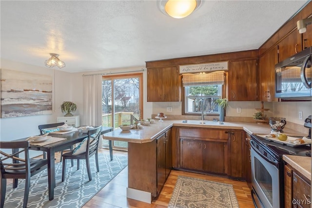 kitchen featuring kitchen peninsula, light wood-type flooring, a textured ceiling, stainless steel appliances, and sink