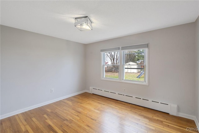 spare room featuring baseboard heating and light hardwood / wood-style floors