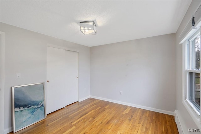 empty room with light wood-type flooring and a baseboard heating unit