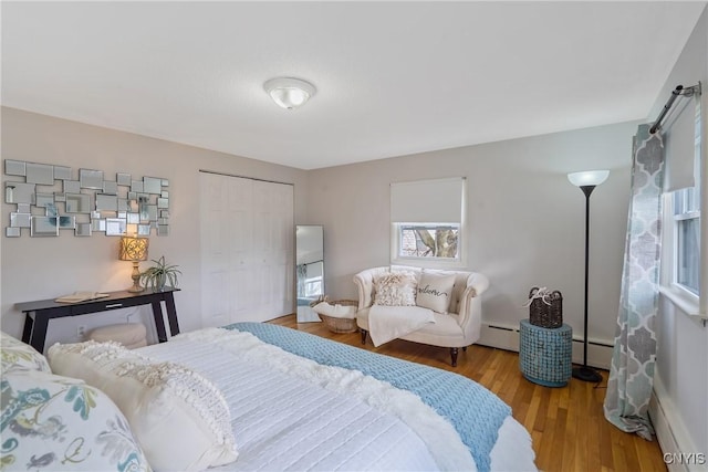 bedroom featuring light wood-type flooring, baseboard heating, and a closet