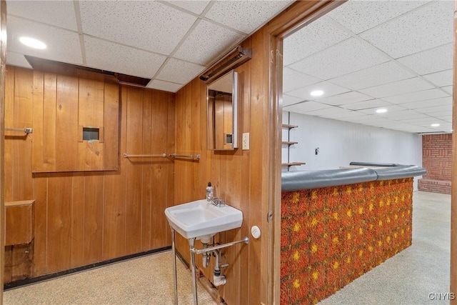 bar featuring light carpet, sink, a drop ceiling, and wood walls