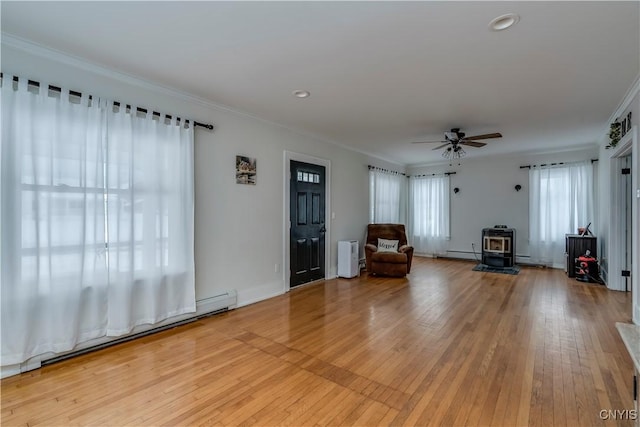 unfurnished room featuring light wood-type flooring, ornamental molding, ceiling fan, a baseboard radiator, and a wood stove